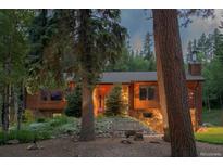 Charming wood and stone home featuring mature trees, front bench, and lovely landscaping at 1345 Witter Gulch Rd, Evergreen, CO 80439