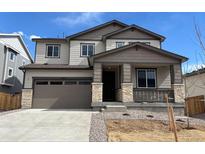 Two-story home with brown accents, a two-car garage, stone pillar accents, and a covered porch at 9082 Telluride Ct, Commerce City, CO 80022