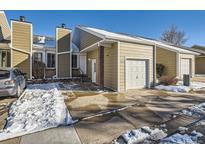 Tan siding townhouse with white door, attached garage, and snow-covered walkway at 11860 Harrison St, Thornton, CO 80233