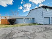 View of the side of the house, showing the garage, the meter, and the yard, with bright blue sky above at 1049 W 112Th Ave # A, Denver, CO 80234