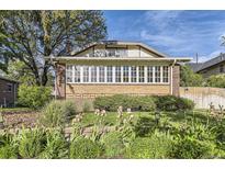 Charming brick home featuring a wall of windows and landscaped front yard with colorful flowers, creating inviting curb appeal at 1230 S Emerson St Dr, Denver, CO 80210