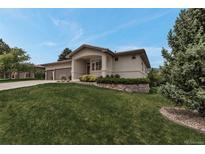 Beautiful stucco home featuring a well-maintained lawn, mature trees, and a stone garden bed at 6379 Spotted Fawn Run, Littleton, CO 80125