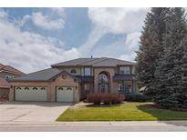 Two-story brick home featuring a three-car garage and mature landscaping on a sunny day at 116 Willowleaf Dr, Littleton, CO 80127
