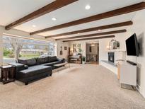 Bright living room featuring exposed wood beam ceilings, a fireplace, and a large picture window at 7105 Dover Way, Arvada, CO 80004