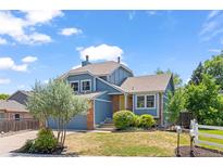 Charming blue two-story home featuring a well-manicured lawn, brick accents, and a lovely garden with mature landscaping at 9917 Garland Dr, Broomfield, CO 80021