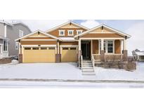 Charming brown two-story home featuring a two-car garage and inviting front porch, surrounded by a snowy landscape at 19473 W 58Th Pl, Golden, CO 80403