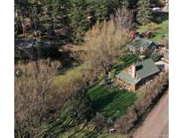 Charming log cabin with green roof nestled in a wooded area with a well-manicured lawn at 5502 Santa Clara Rd, Indian Hills, CO 80454