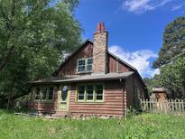 Charming wood home featuring a stone chimney, green trim, and mature trees, creating a cozy, rustic appeal at 5502 Santa Clara Rd, Indian Hills, CO 80454