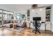 Comfortable living area featuring a gray sectional sofa, hardwood floors, and a built-in Murphy bed with shelving and desk at 790 N Washington St # 1003, Denver, CO 80203