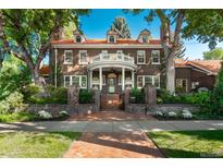 Elegant brick home featuring a rounded balcony, red tile roof, mature trees, and landscaped front yard at 3309 E 7Th Ave Pkwy, Denver, CO 80206