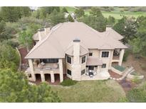 Expansive rear exterior showcasing a covered patio, manicured lawn, and mature landscaping with views of a golf course at 214 Equinox Dr, Castle Rock, CO 80108