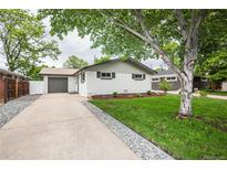 Charming ranch-style home features a well-maintained lawn, mature tree, and a driveway leading to an attached garage at 320 S Jersey St, Denver, CO 80224