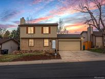Two-story home with a two-car garage, brick facade, tan siding, and a manicured front yard at sunset at 18093 E Milan Pl, Aurora, CO 80013