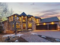 Stunning stone house with three-car garage, basketball hoop, and manicured front yard, illuminated by twilight at 5810 Amber Ridge Dr, Castle Pines, CO 80108