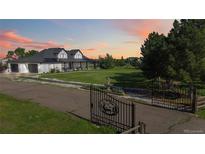 Charming two-story home with a large front yard, gated entry, and beautiful landscaping at sunset at 1550 Ajax St, Strasburg, CO 80136