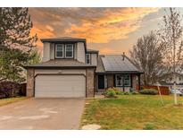 Charming two-story home with a brick-accented garage, solar panels and well-manicured front lawn against a colorful sunset at 6647 Lynx Cv, Lone Tree, CO 80124