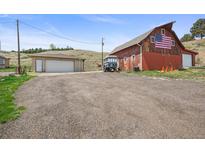 Spacious red barn with an American flag and a detached garage on a large lot with a gravel driveway at 12101 Riverdale Rd, Brighton, CO 80602