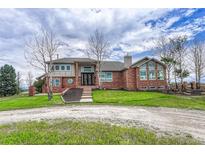 Spacious brick home featuring a well-manicured lawn and ample natural light, with mature trees lining the property at 1820 S State 83 Hwy, Franktown, CO 80116