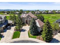 An aerial view of a landscaped two-story home, with a circular driveway, on a golf course near the mountains at 1287 Buffalo Ridge Rd, Castle Pines, CO 80108