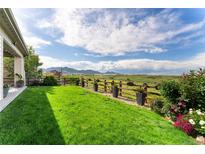 Expansive backyard featuring lush lawn, flower beds, and a wood fence with potted plants, set against a scenic mountain view at 19429 W 88Th Dr, Arvada, CO 80007