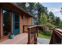 Inviting front porch with a blue door, wooden decking and railing, and serene wooded views at 29101 Drexel Spur, Evergreen, CO 80439