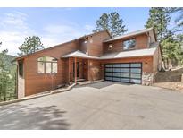 Beautiful two-story home with brown wood exterior and a contemporary glass-paneled garage door at 7395 Heiter Hill Dr, Evergreen, CO 80439