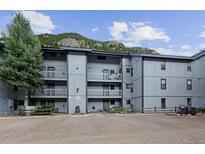 Three-story condominium with grey wood, balconies, gravel parking, and view of mountains in the background at 1901 Clear Creek Dr # F104, Georgetown, CO 80444