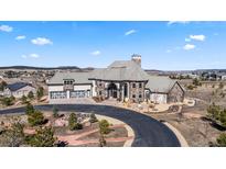 Elegant home featuring stone and siding exterior, a three-car garage, and beautiful landscaping on a sunny day at 19205 Sixpenny Ln, Monument, CO 80132