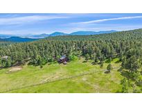Stunning aerial view of a home nestled in a verdant meadow surrounded by trees and rolling hills at 26085 Amy Cir, Conifer, CO 80433