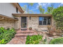 Welcoming brick home featuring a covered porch, mature landscaping, and an inviting front door at 10165 W Iowa Ave, Lakewood, CO 80232