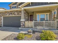 Inviting front porch with stone accents, decorative fencing and dark colored garage at 458 Highlands Cir, Erie, CO 80516