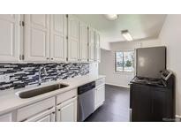Bright kitchen featuring white cabinetry, a stainless steel dishwasher, and mosaic tile backsplash at 2865 S Fairfax St, Denver, CO 80222
