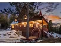 Charming wood home with a covered porch, lush evergreens, and snow-covered yard at dusk at 439 Ronnie Rd, Golden, CO 80403
