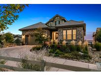 Charming stone home with a well-manicured front yard and a curved driveway at dusk at 10731 Featherwalk Ln, Highlands Ranch, CO 80126