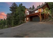 Two-story wood home with a drive-under garage, large windows, and a wrap-around balcony at 11760 Baca Rd, Conifer, CO 80433