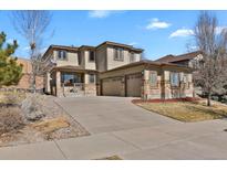 A tan two-story home with a three-car garage, brick accents, and a concrete driveway under a blue sky at 24269 E Arapahoe Pl, Aurora, CO 80016