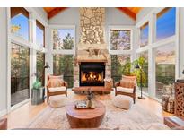 Inviting living room with stone fireplace, wood accents, and many large windows overlooking wooded exterior at 5090 S Perry Park, Sedalia, CO 80135