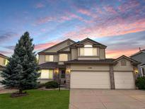 Two-story home with a three-car garage, green lawn, and a large pine tree under a colorful sky at 15498 E Dorado Pl, Centennial, CO 80015