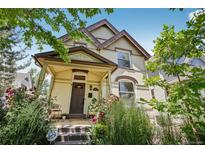 Charming two-story home with a covered porch, mature trees, and colorful flowers surrounding the entrance at 351 Bannock St, Denver, CO 80223