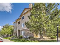 Inviting multi-story condo building featuring a mix of stone and vinyl siding, mature trees and manicured lawn at 8445 S Holland Way # 205, Littleton, CO 80128