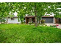 Charming single-story home with a well-manicured lawn, lush trees, and a beautifully painted white brick exterior at 3125 Xenon St, Wheat Ridge, CO 80215