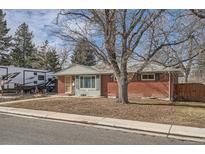 Charming brick home featuring a cozy front yard with mature trees and a small seating area at 7005 S Ash Cir, Centennial, CO 80122