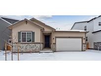 Tan house with stone accents, a two-car garage, and landscaping; winter scene at 144 Wooten Ave, Brighton, CO 80601