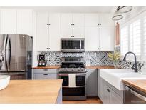 Bright kitchen features stainless steel appliances, farmhouse sink, patterned backsplash, and light countertops at 2719 S Truckee St, Aurora, CO 80013