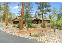Stunning wood and stone home with rock landscaping and a brick retaining wall in a wooded area at 7597 Molas Ct, Larkspur, CO 80118