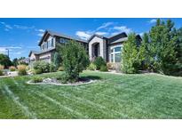 Beautifully landscaped front yard with a lush lawn, mature trees, and a stately two-story residence with a three-car garage at 7408 Sodalite Way, Castle Rock, CO 80108