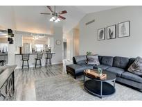 Open-concept living room featuring a gray sofa, vaulted ceilings, and a breakfast bar overlooking the kitchen at 4108 S Rifle Way, Aurora, CO 80013