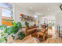 Bright living room features a brown leather sofa, hardwood floors, and stylish decor with a view into the open concept dining area at 1833 E Jewell Ave, Denver, CO 80210