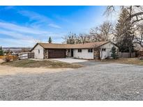 Charming single-story house featuring a stone and siding exterior, brown roof, and an expansive gravel driveway at 14290 W 54Th Ave, Arvada, CO 80002