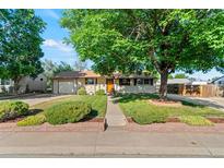 Charming ranch-style home with a well-manicured lawn and a mature tree, perfect curb appeal with an orange front door at 7310 Granada Rd, Denver, CO 80221